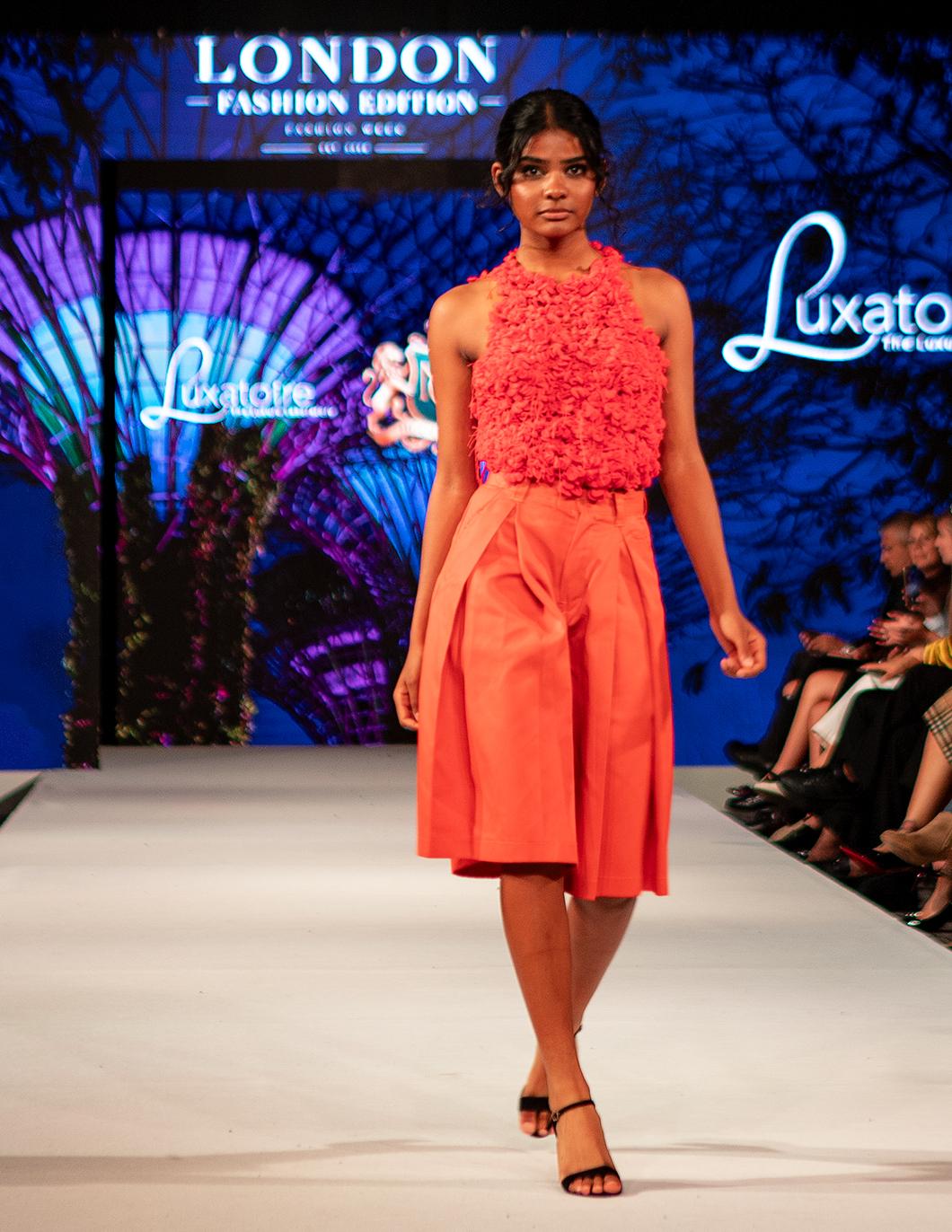 Model wearing a coral LUXATOIRE design on the London runway
