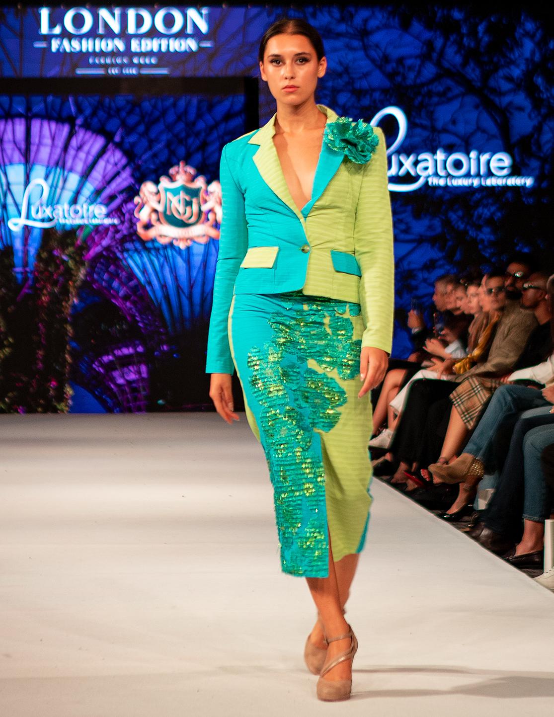 Model wearing a turquoise and green LUXATOIRE design on the runway in London